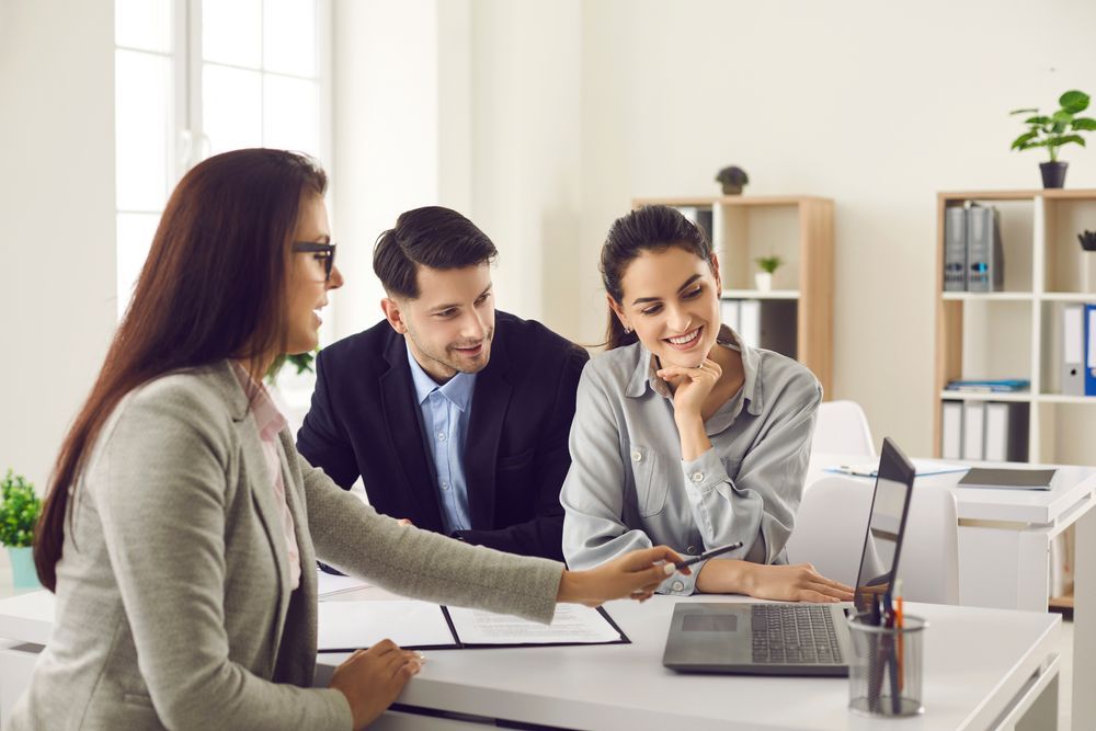 A Woman Points at a Laptop Screen While Consulting With a Couple in an Office — Adamson Town Planning in Noosaville, QLD