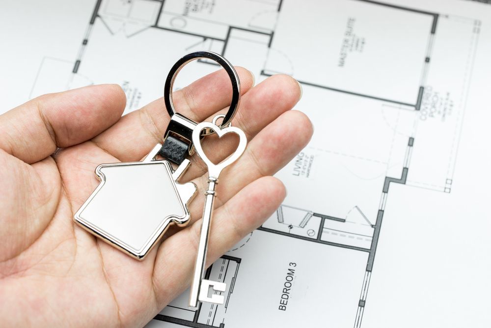 Hand Holding House Key and Heart Key Ring Over a Home Blueprint — Adamson Town Planning in Noosaville, QLD