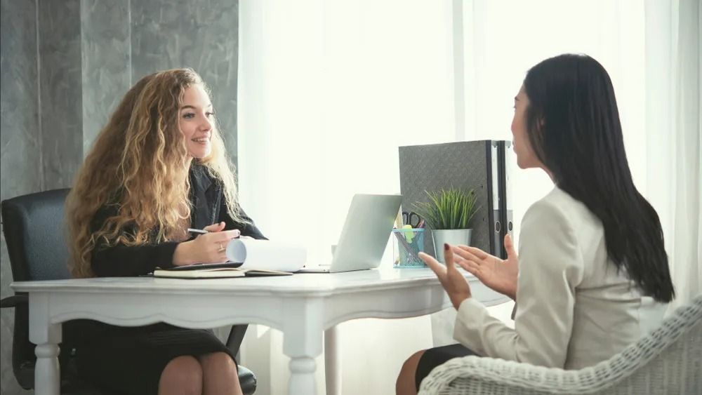 Two Women in a Bright Office Meeting, Seated Across a White Table — Adamson Town Planning in Noosaville, QLD