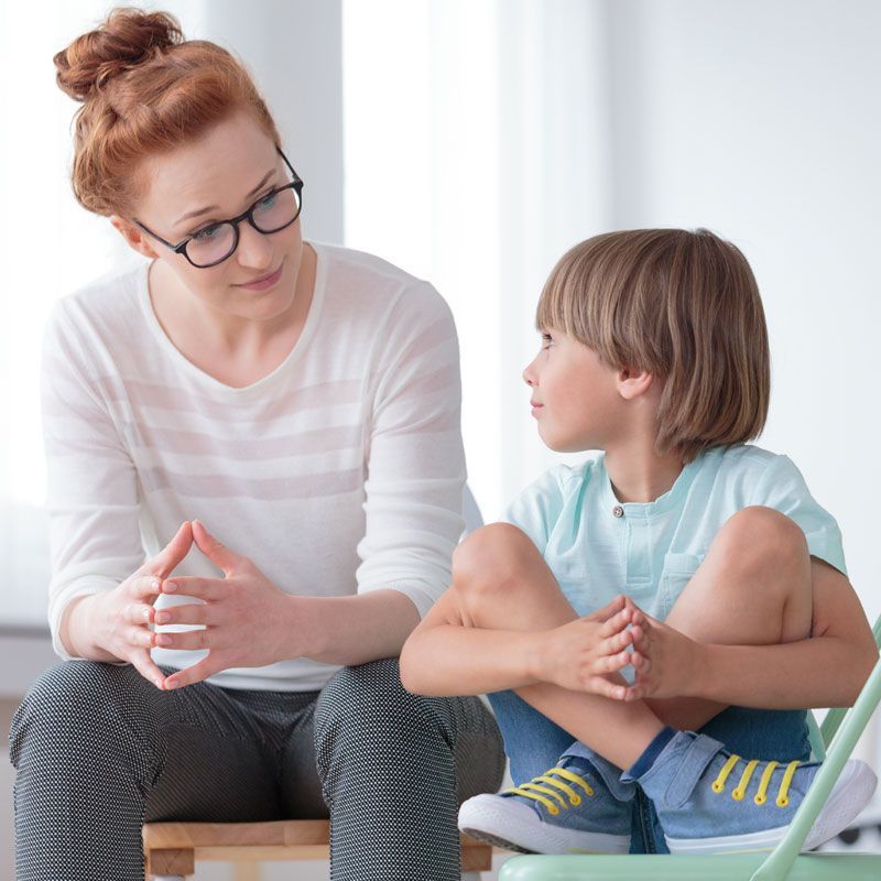 A woman is sitting on a chair talking to a young boy.