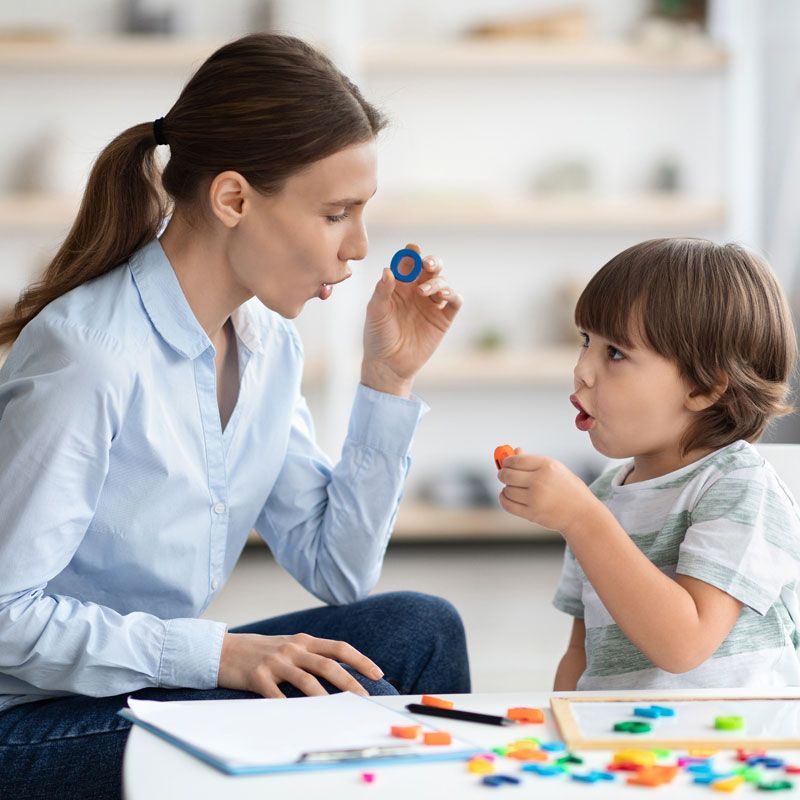 A woman is sitting at a table talking to a little boy.