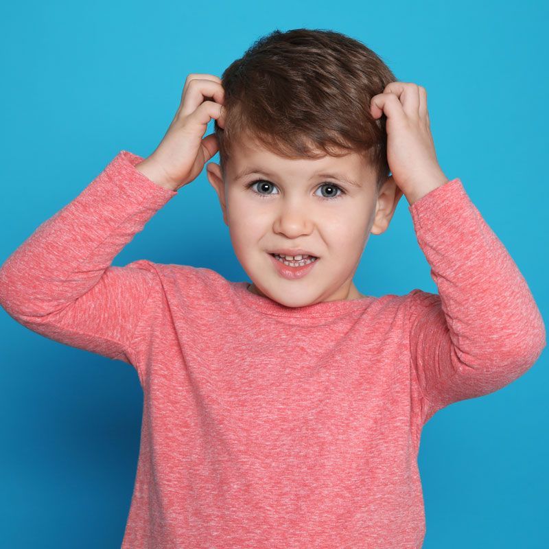 A young boy in a pink shirt is scratching his head against a blue background.