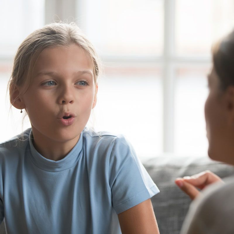 A young girl is sitting on a couch talking to a woman.