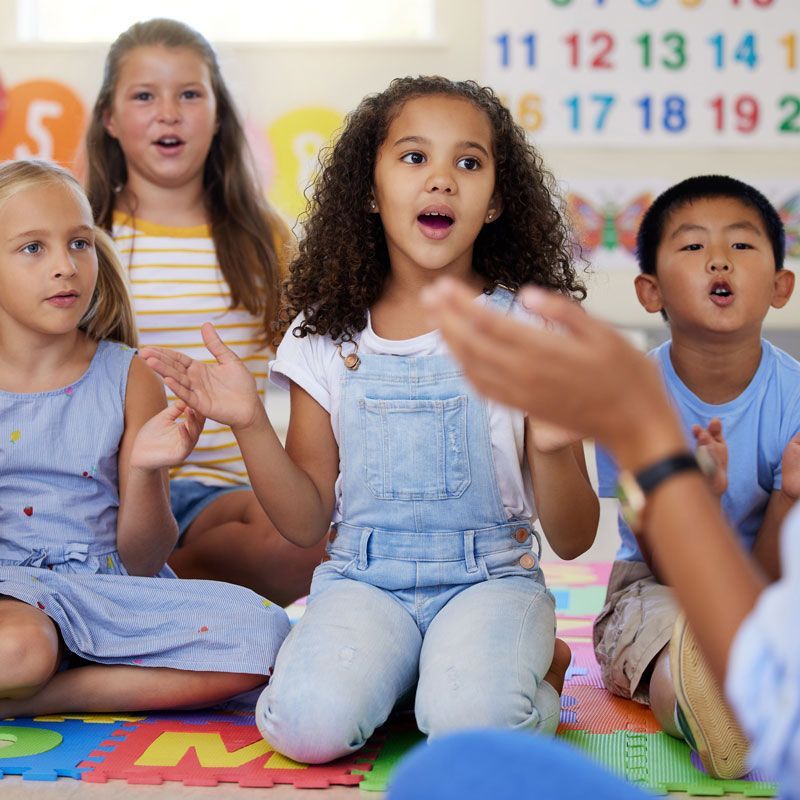 A group of children are sitting on the floor in front of a wall with numbers on it