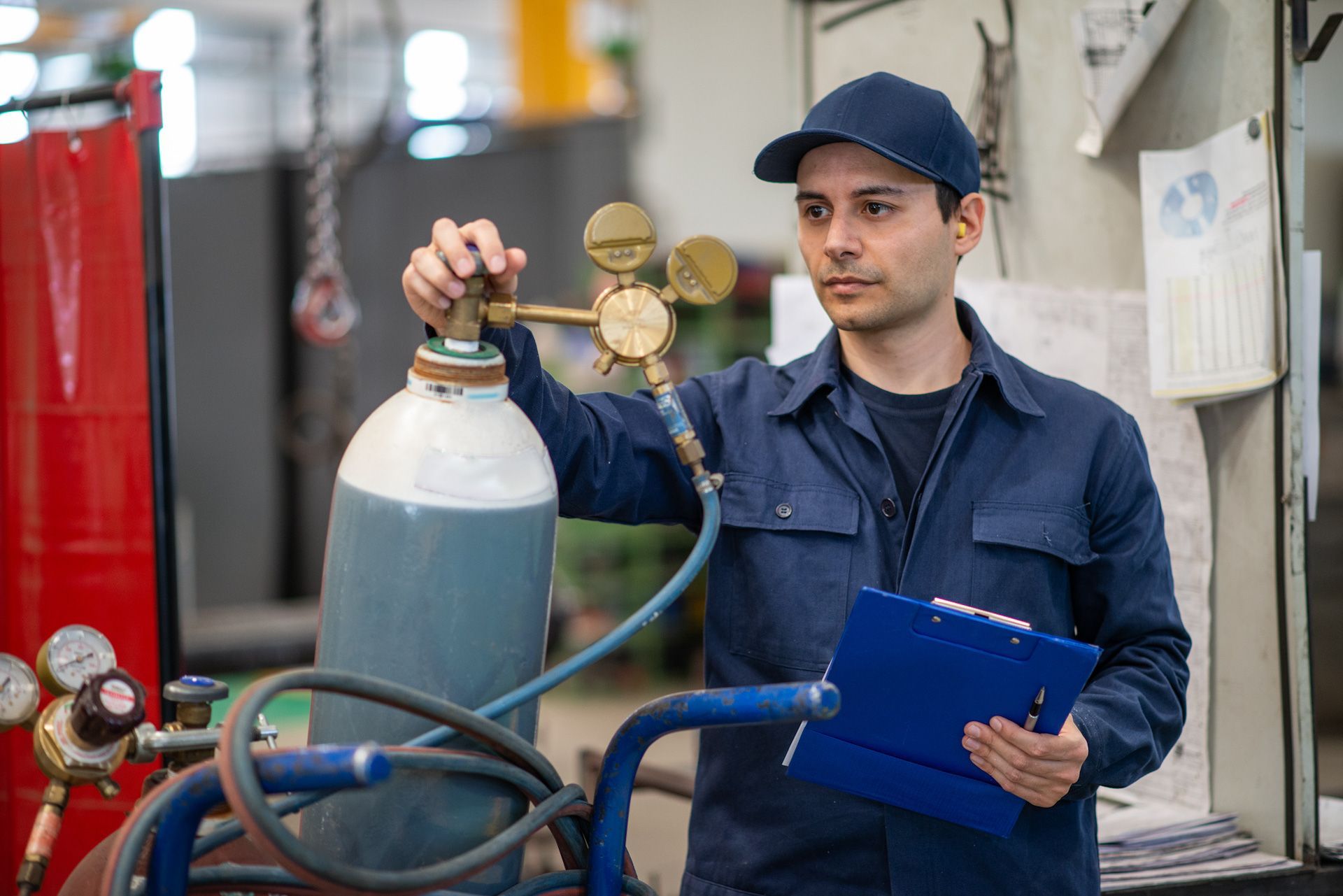 A man is working on a gas cylinder in a factory while holding a clipboard