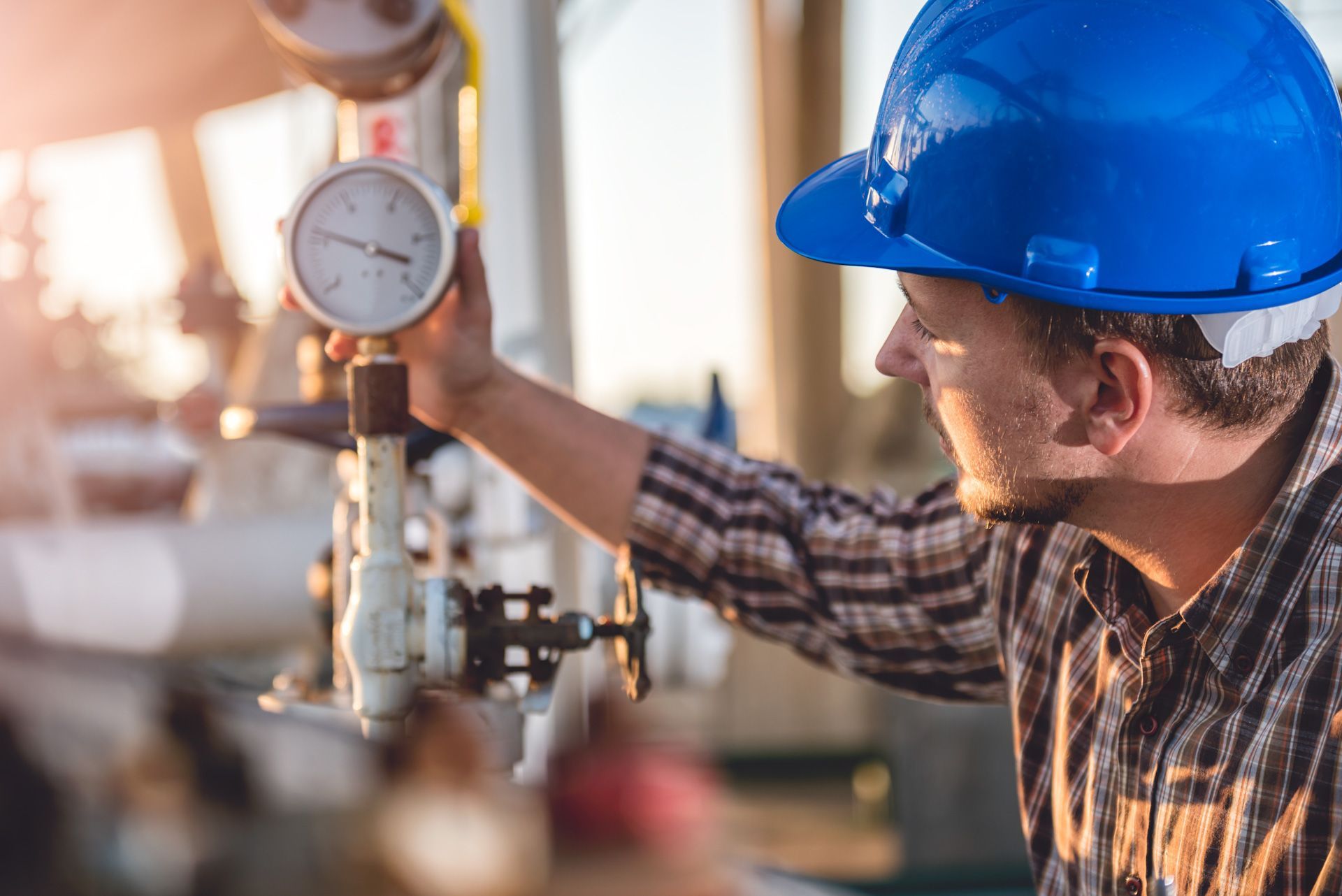 A man wearing a blue hard hat is holding a pressure gauge