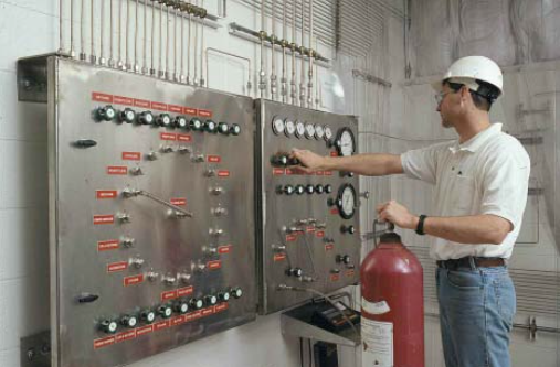 A man is holding a red fire extinguisher in front of a control panel.
