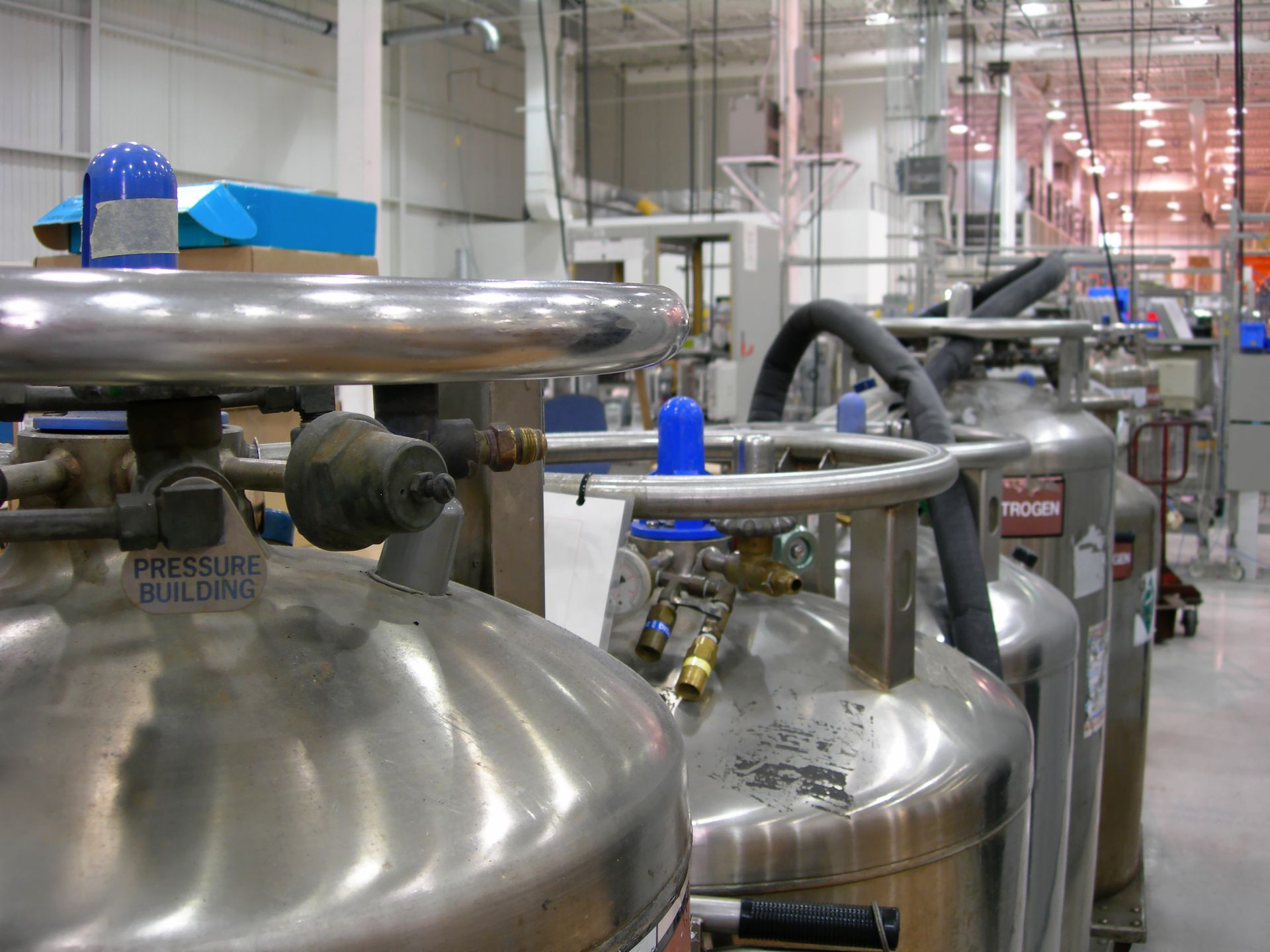 A row of stainless steel tanks are lined up in a factory.