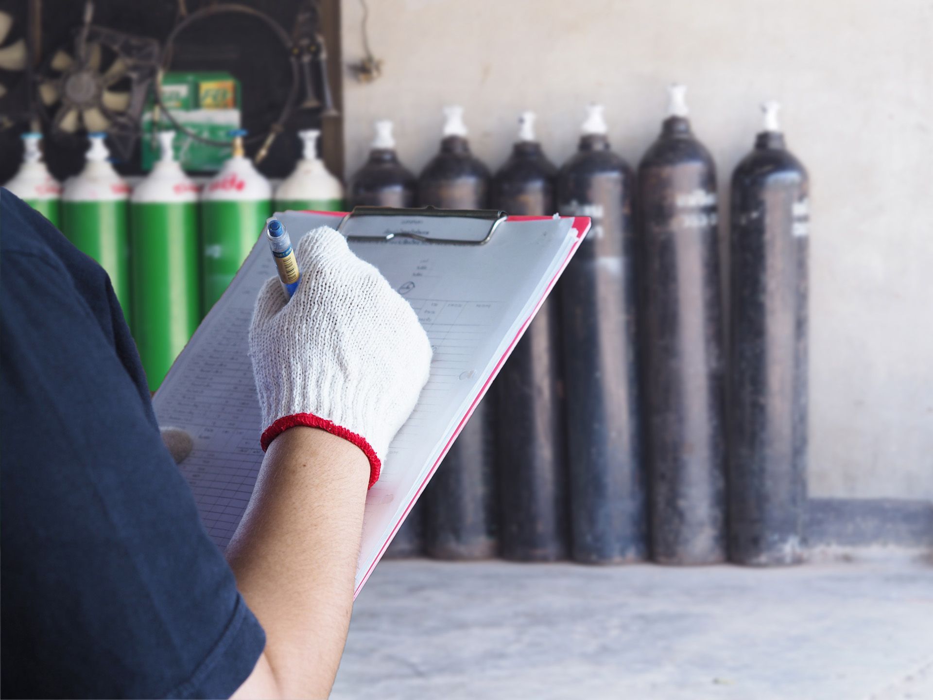A person is writing on a clipboard in front of a row of gas cylinders