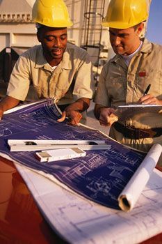 Two construction workers are looking at a blueprint on a table.