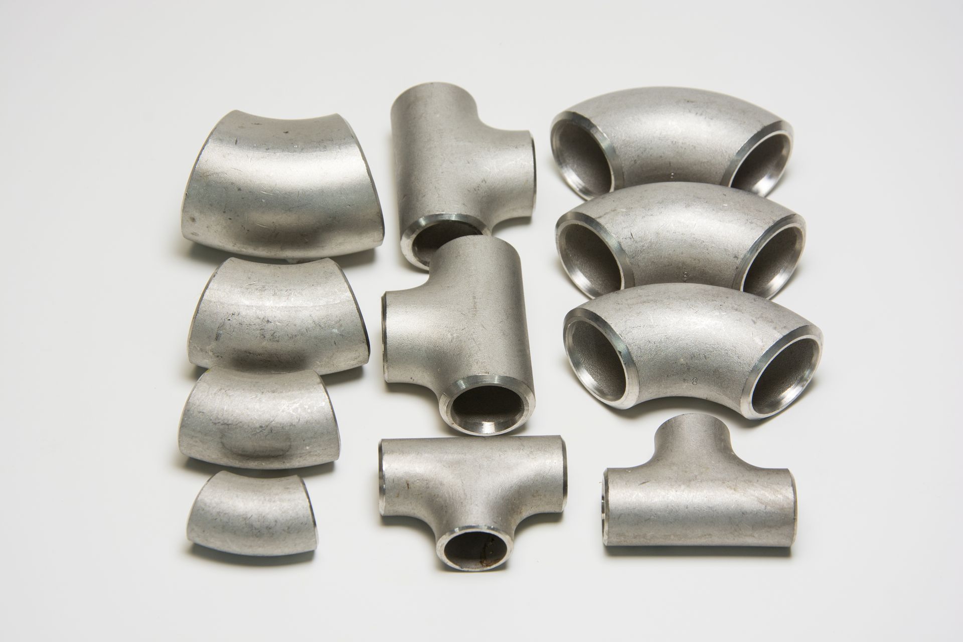 A bunch of stainless steel pipe fittings on a white surface