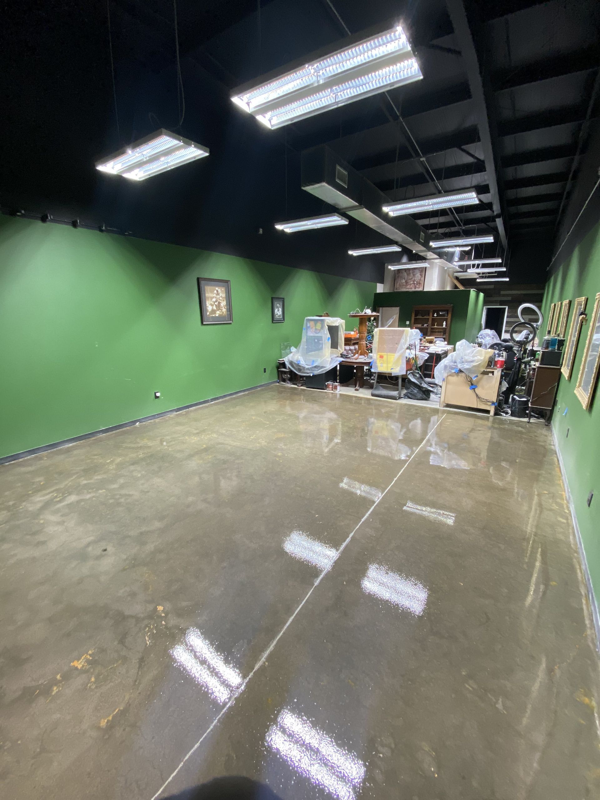 Empty room with green walls, black ceiling, and polished concrete floor. Lighting fixtures are overhead.
