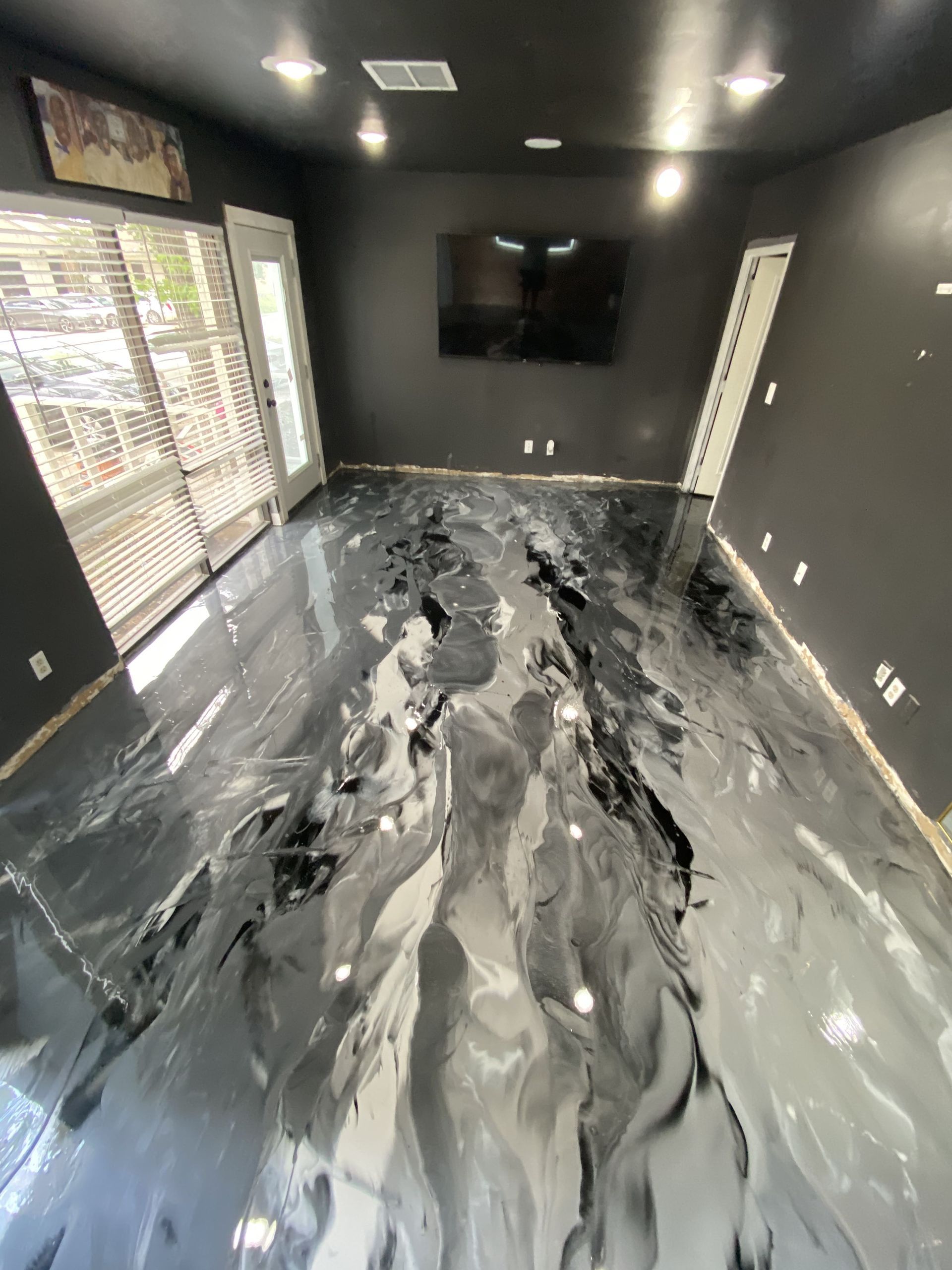 Room with black walls and a glossy black, white, and gray epoxy floor; a TV and open doors are visible.
