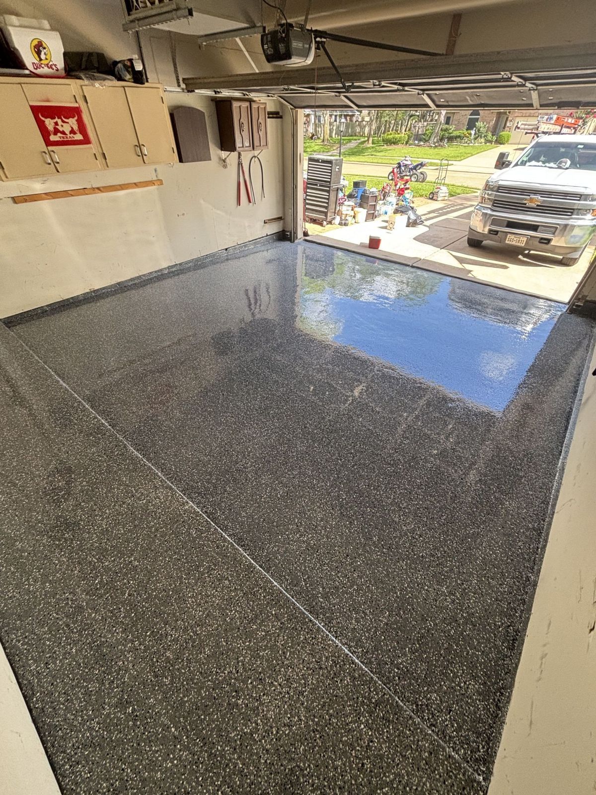 Garage with shiny, speckled gray floor, open to a sunlit outdoor area with a truck.