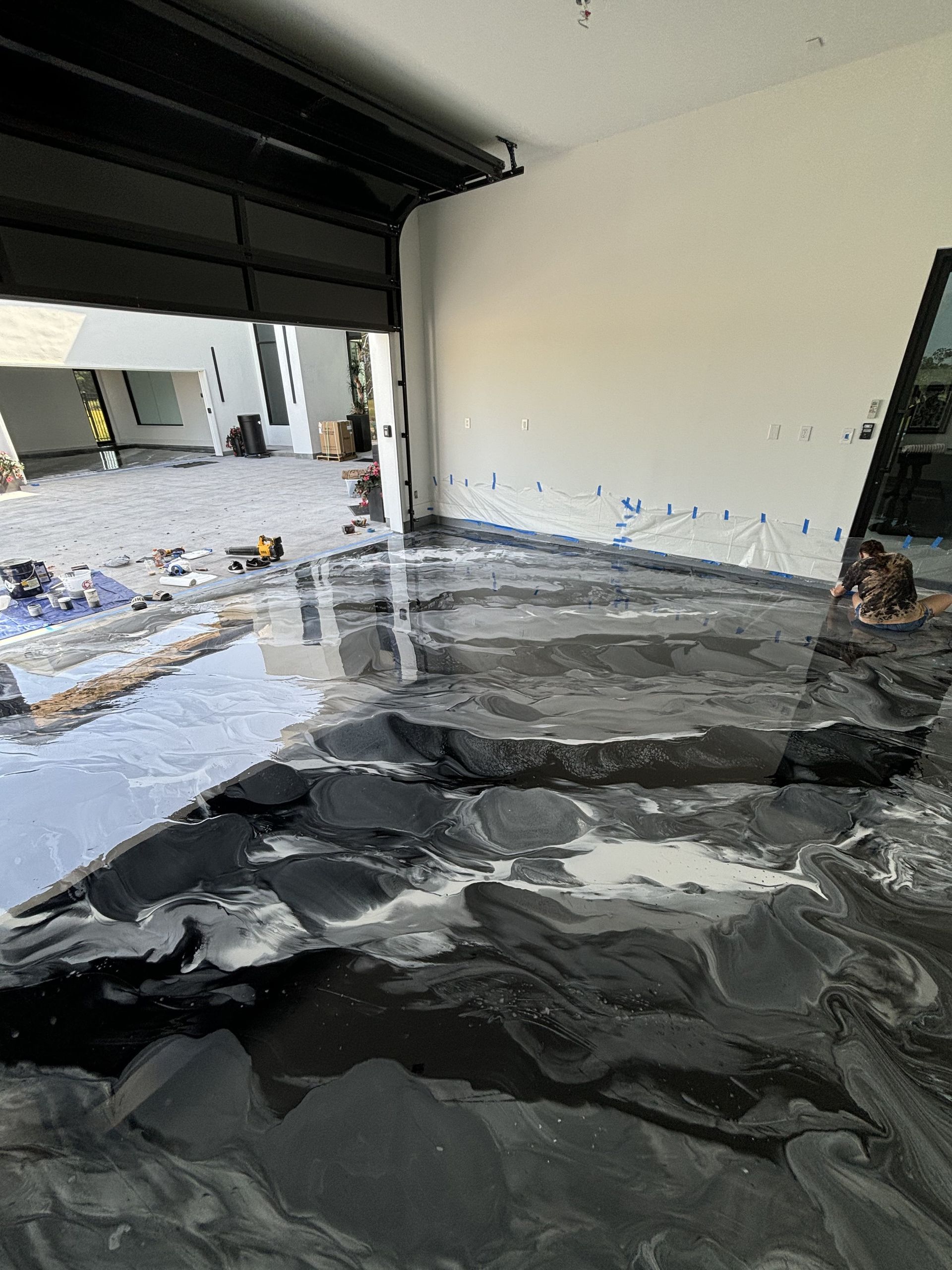 Garage with glossy black epoxy flooring. The garage door is open, with construction in the background.