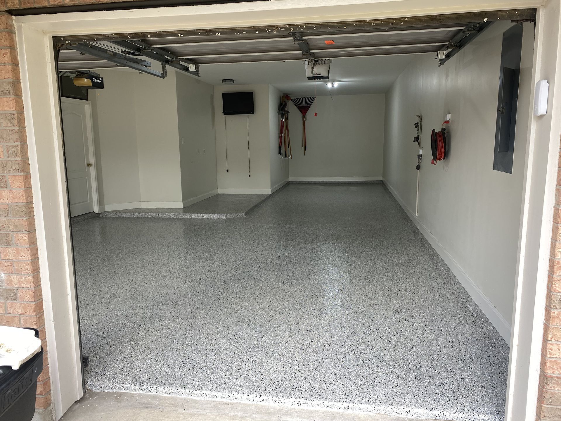Interior view of a clean, empty garage with epoxy floor and open door to the outside.