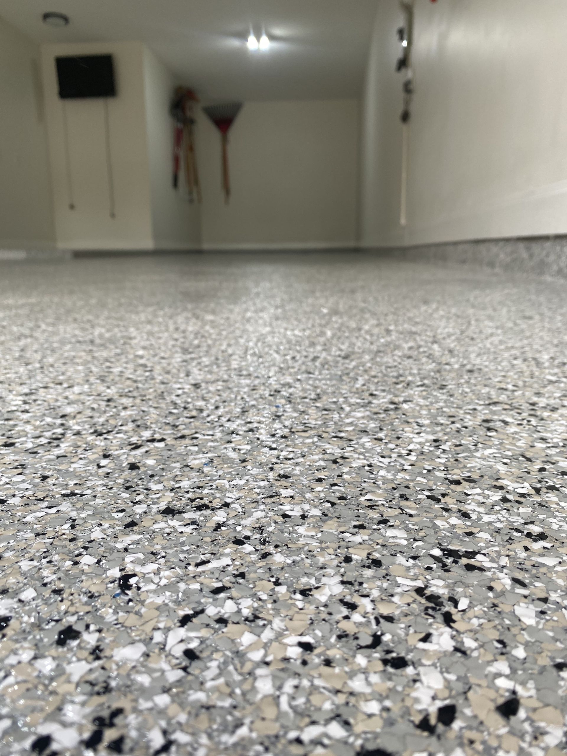 Close-up view of a garage floor with a speckled epoxy coating, various shades of gray and white.