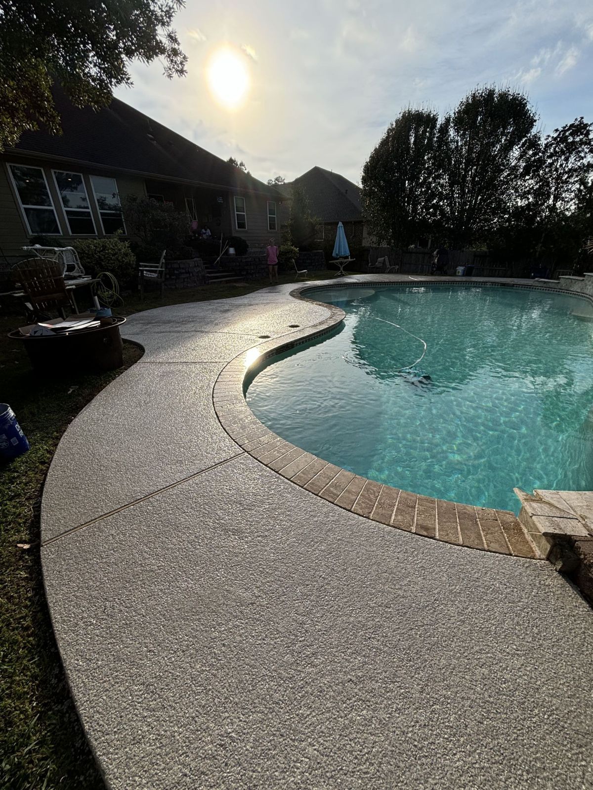Poolside view with concrete walkway, blue water, and sunlight.