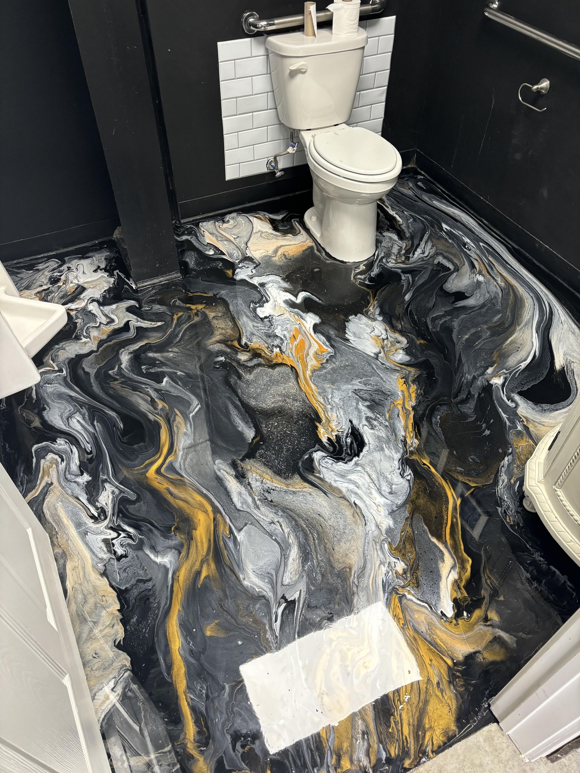 Bathroom floor with black, gold, and white marbled epoxy. Toilet and black walls are also visible.