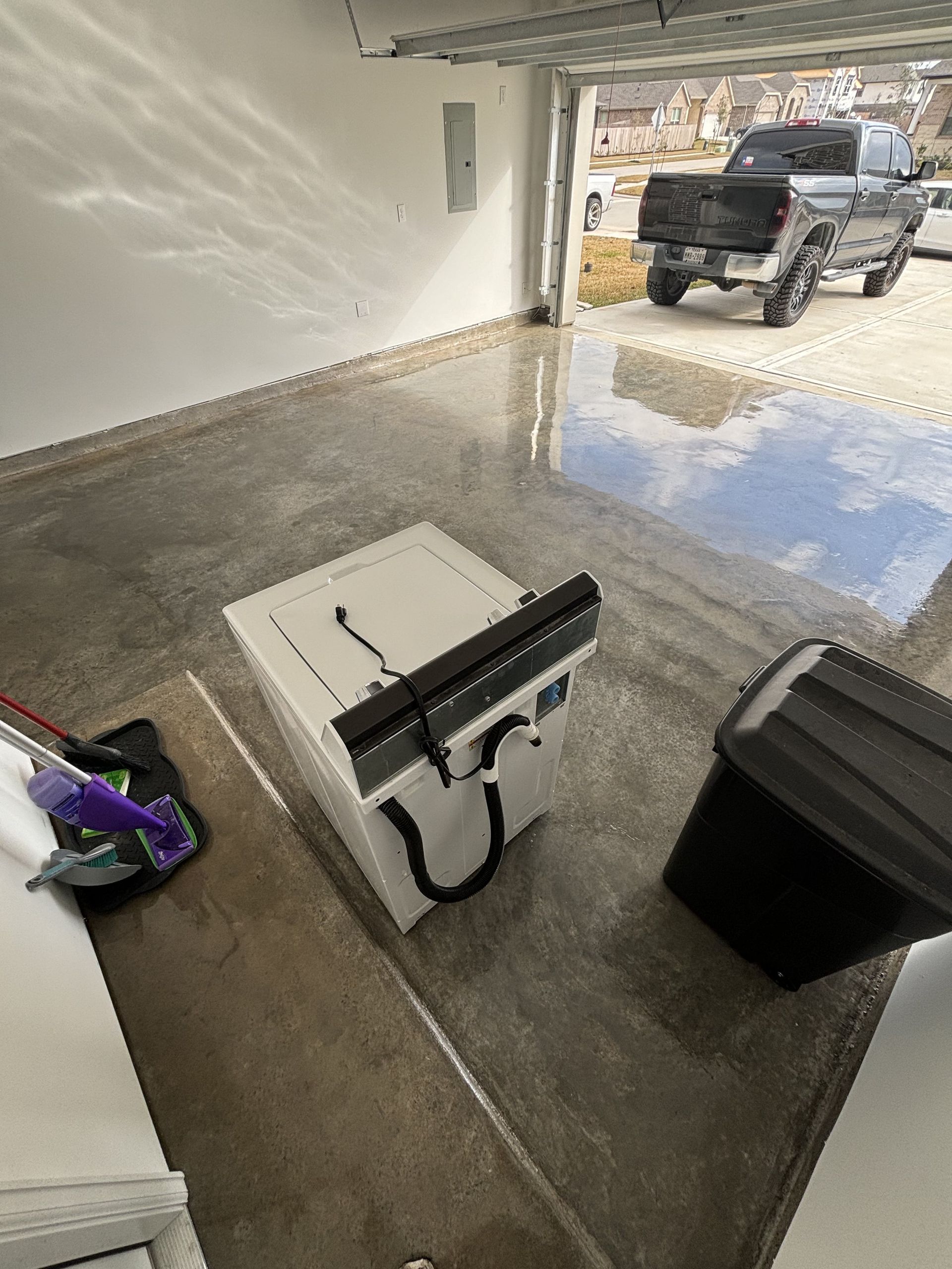 Washing machine and black bin in a garage. A truck is parked outside the open door.