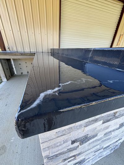 Black countertop with glossy finish, atop a stacked stone base, against a corrugated wall.