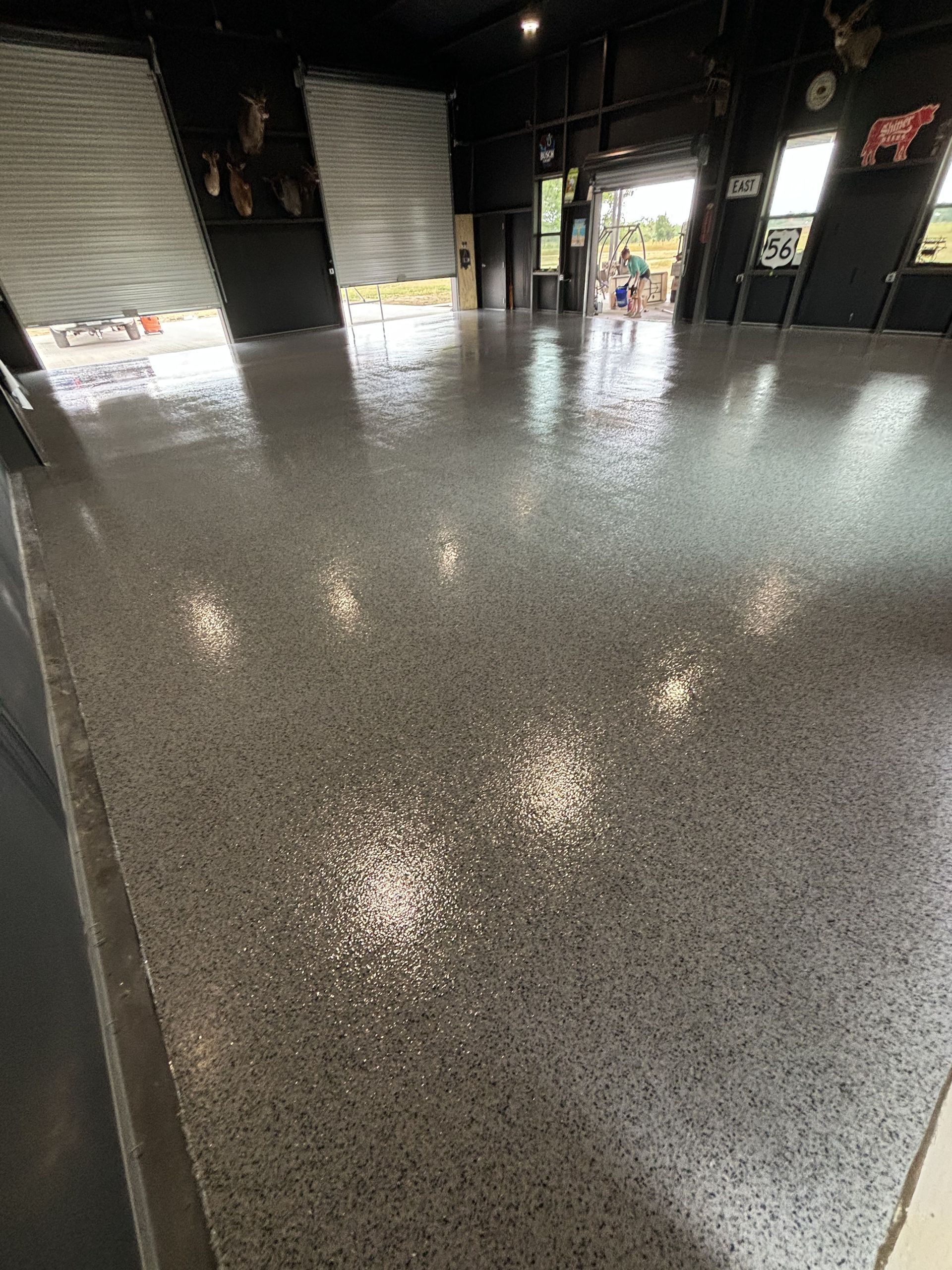 Shiny, gray speckled concrete floor inside a commercial space with open garage doors.