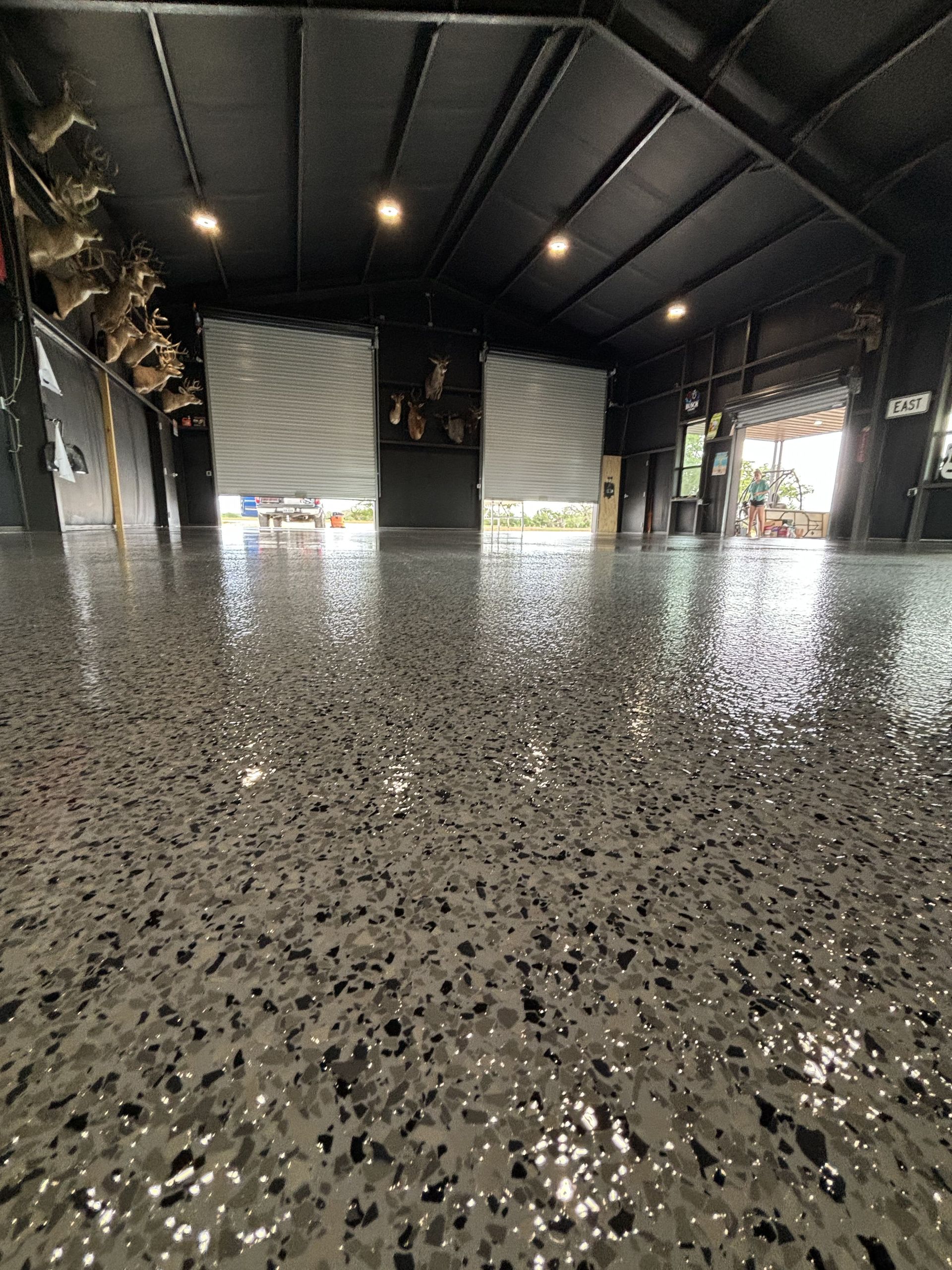 Shiny, speckled gray floor inside a dark building with roll-up doors open to the outdoors.