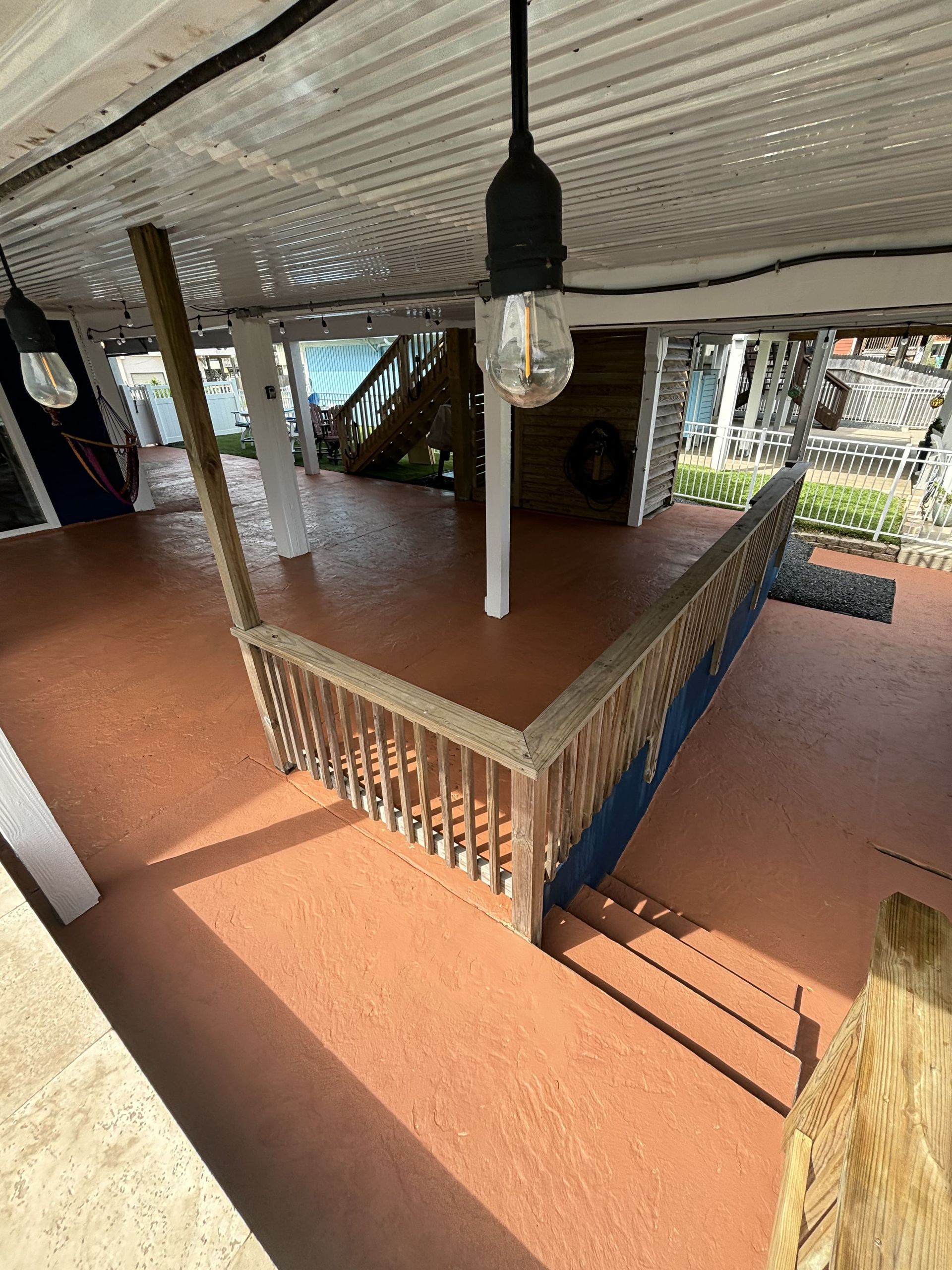 Covered porch with stairs, railing, and terracotta-colored floor. Hanging light fixtures.