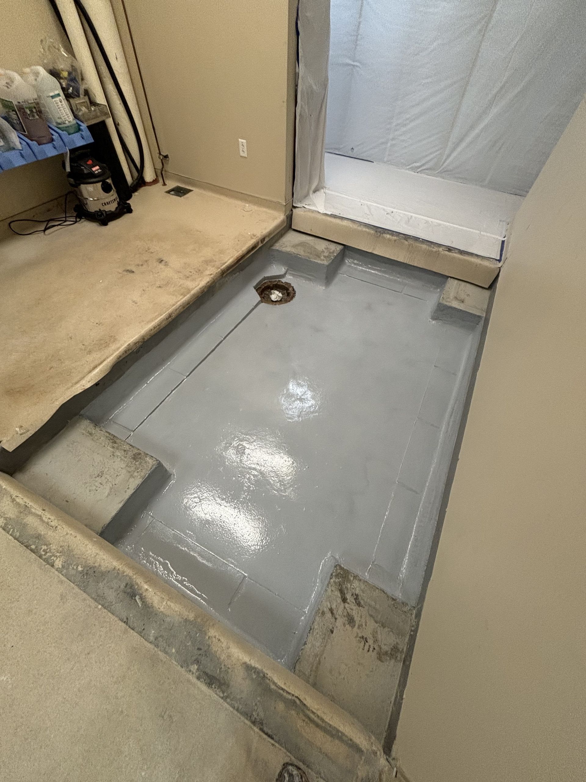 A newly constructed basement floor section with a gray, waterproof coating and a drain.