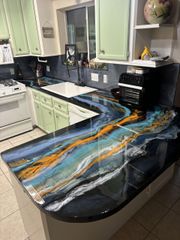 Kitchen countertop with blue, gold, and white resin design; light green cabinets.