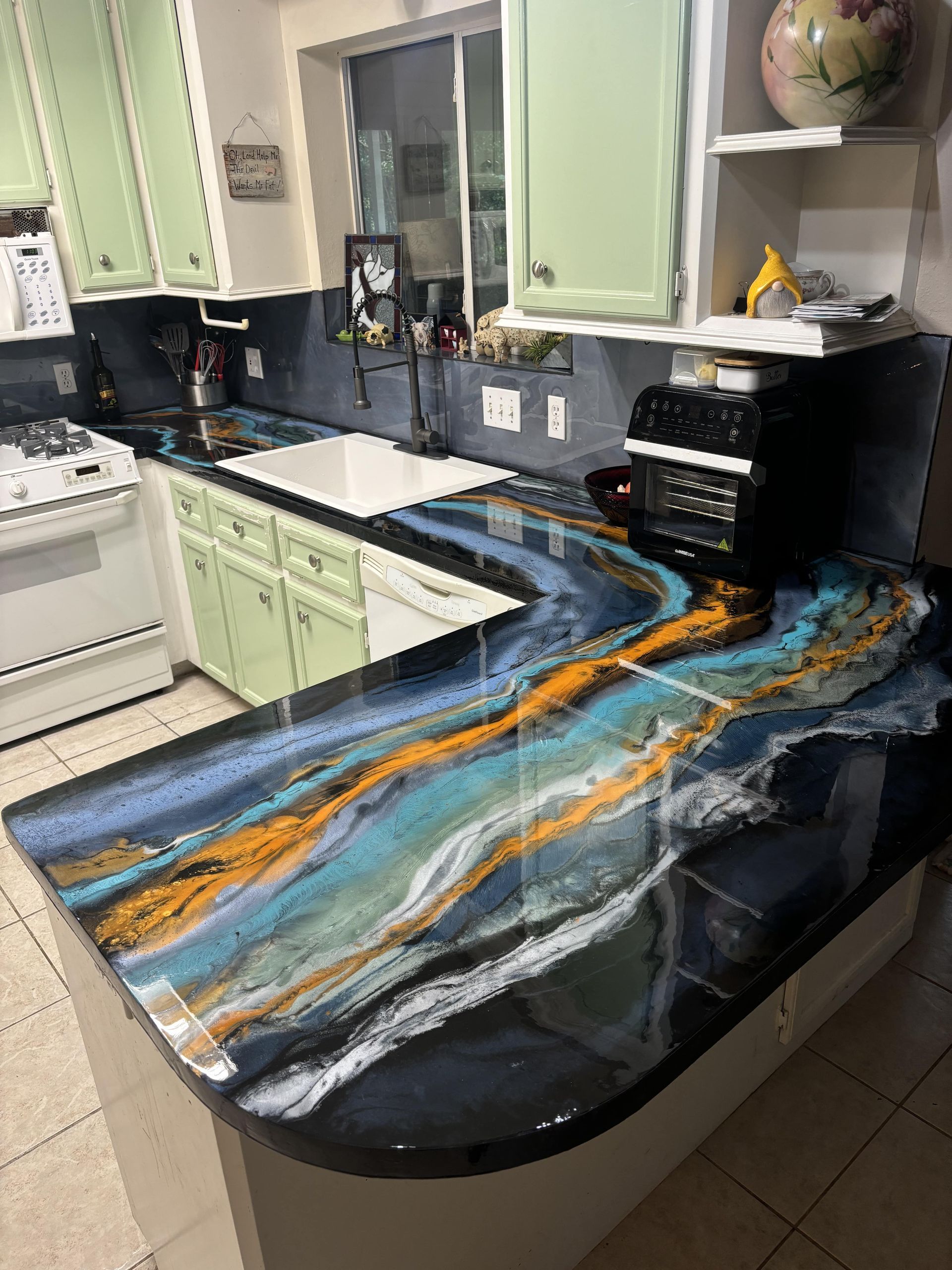 Kitchen countertop with blue, gold, and white resin design; light green cabinets.