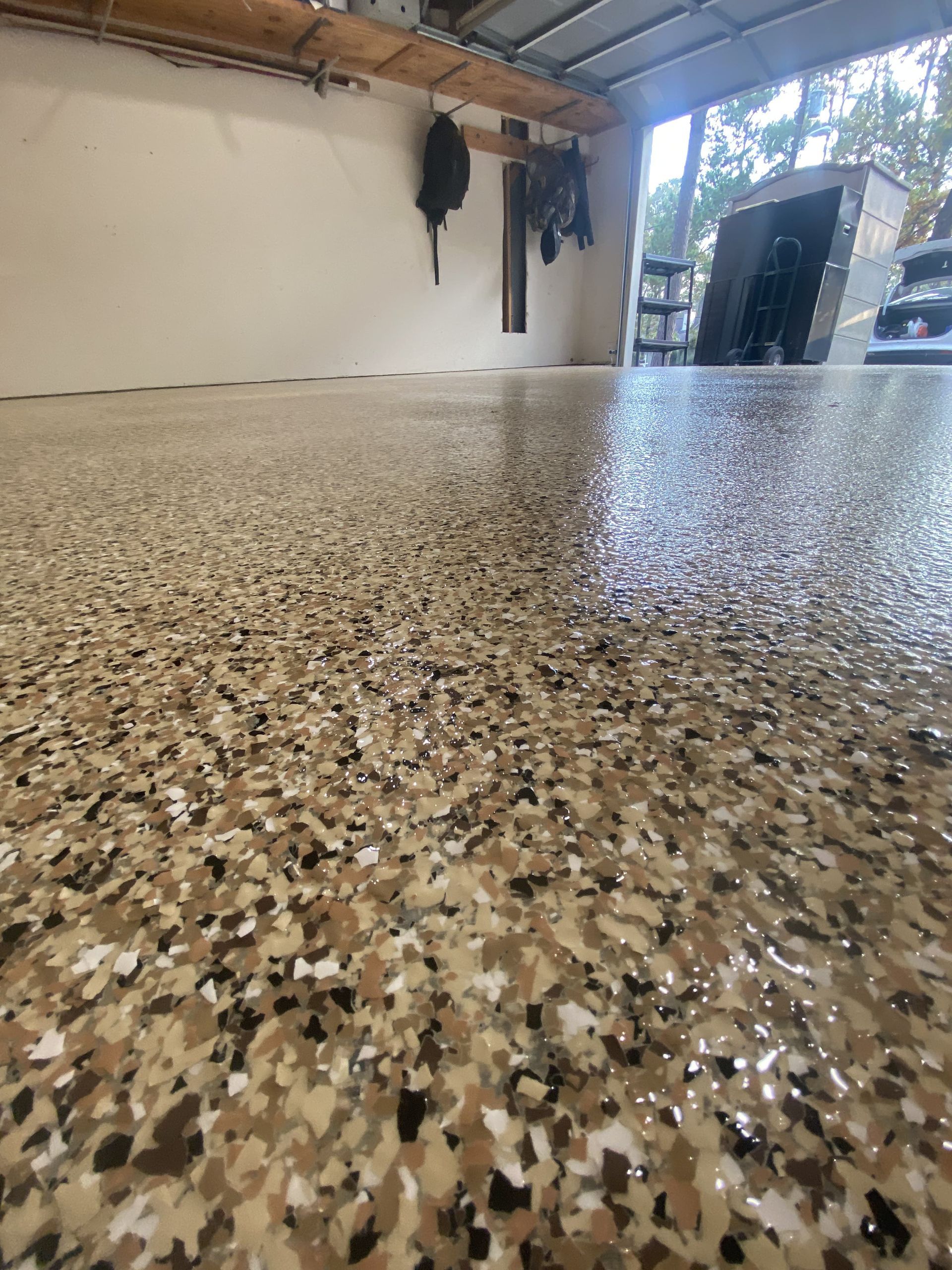 Garage with speckled tan and brown epoxy floor; a partially open garage door.