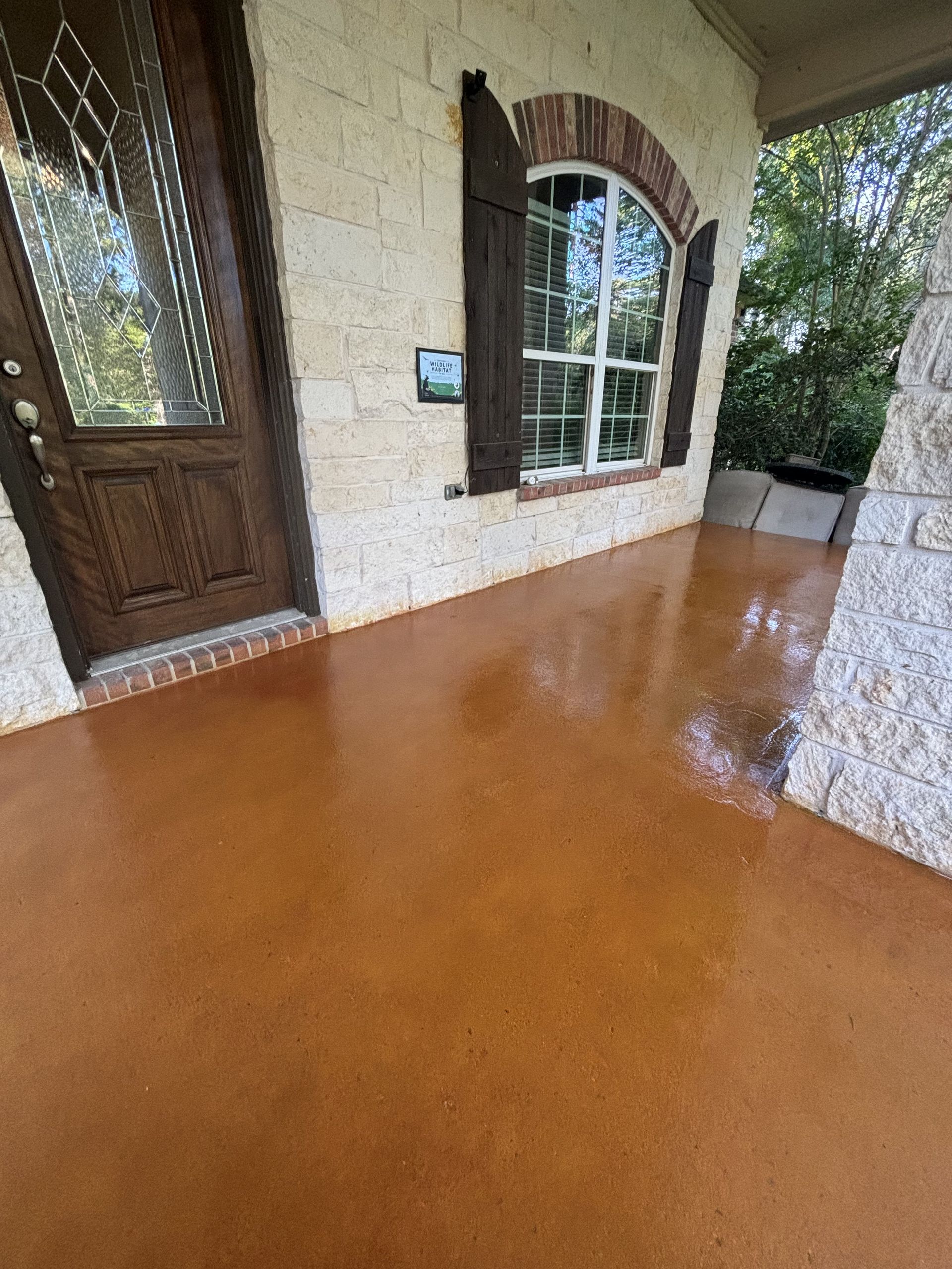 Exterior porch with brown stained concrete floor, door, window, and beige stone wall.