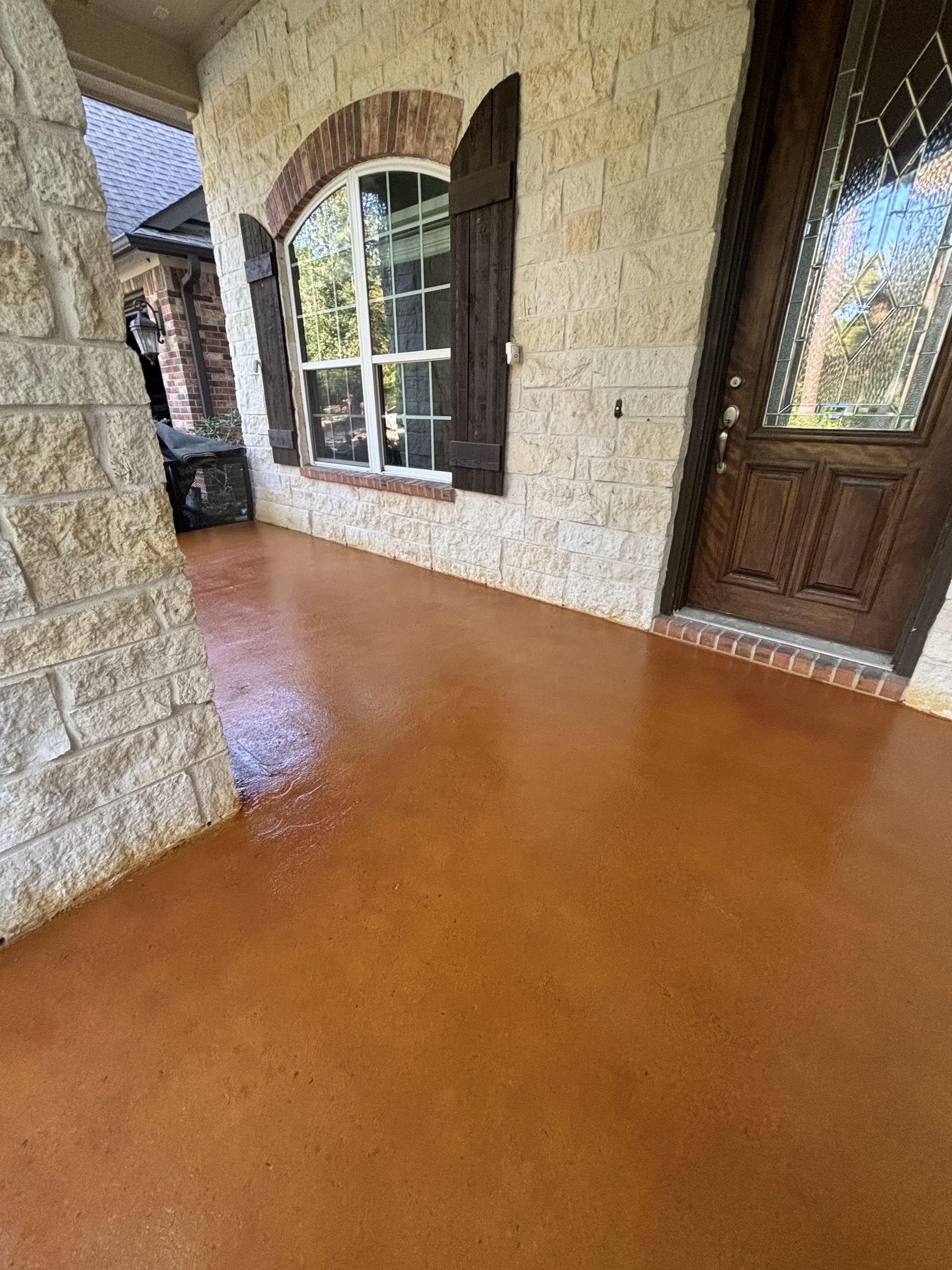 Brown stained concrete porch with stone wall and wooden door.