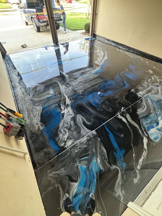 Garage floor with blue, black, and silver epoxy swirl design. Open garage door with person outside.
