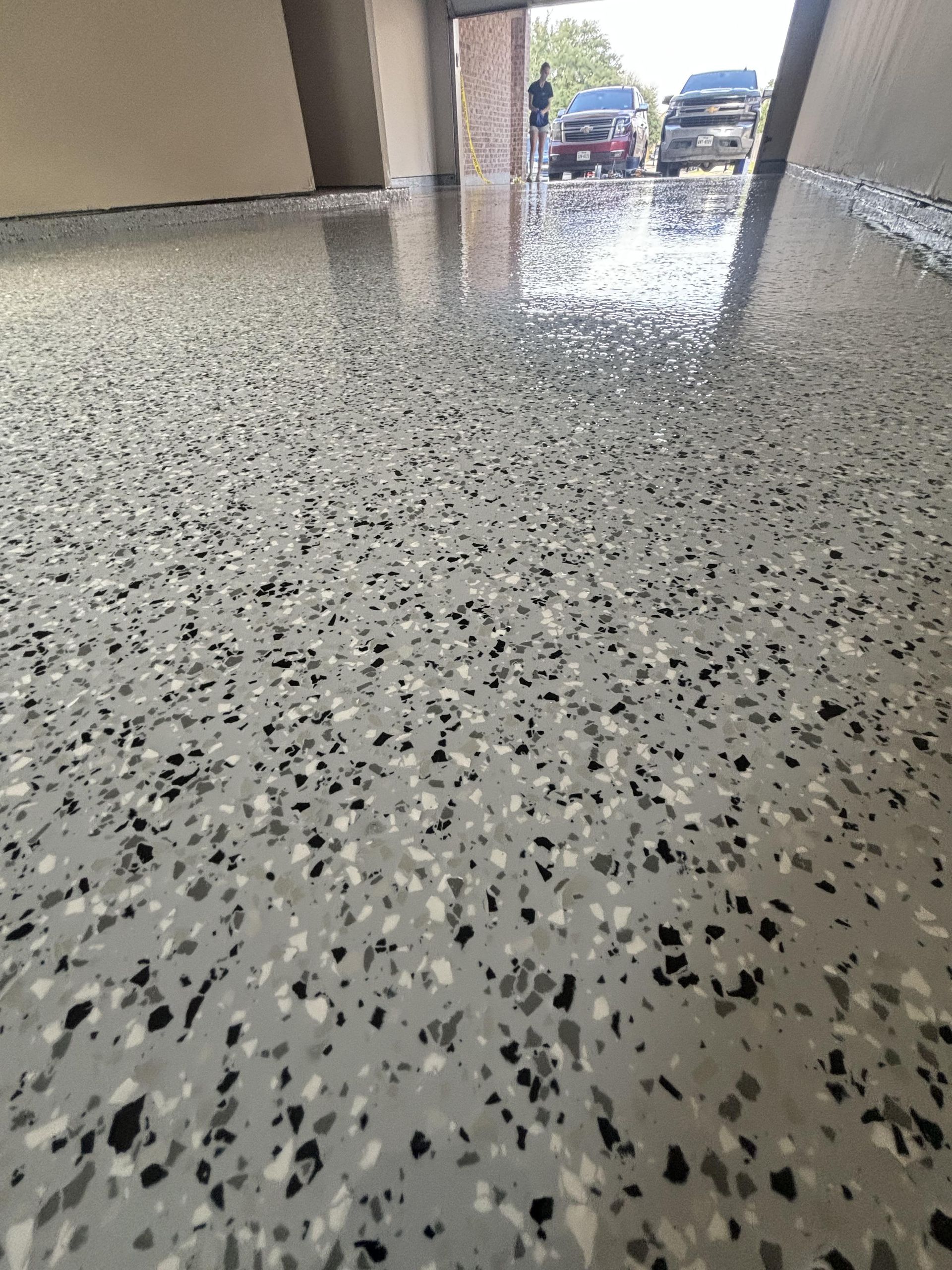 Speckled gray epoxy floor, reflecting sunlight. View of a garage or carport.