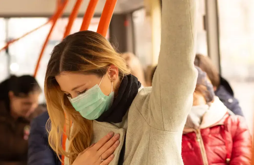 A woman wearing a mask is riding a bus.