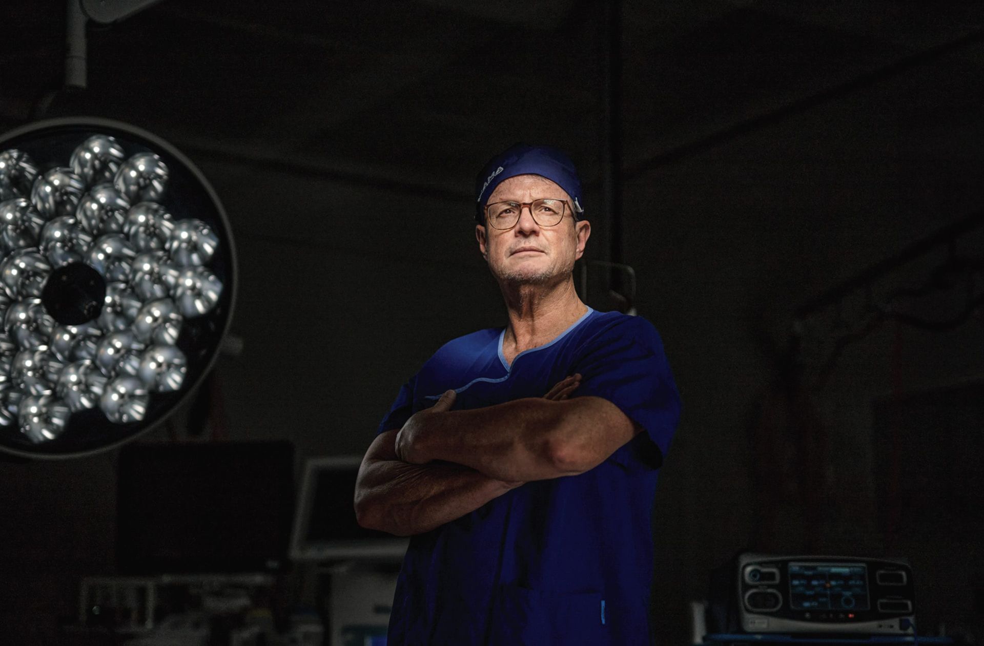 A surgeon is standing in an operating room with his arms crossed.