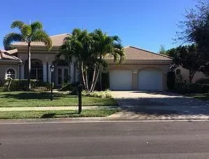 A large house with two garages and palm trees in front of it.
