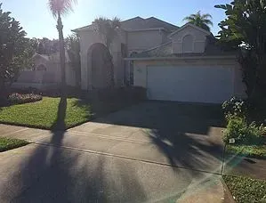 A white house with a garage and a palm tree in front of it.