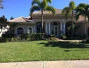 A large house with a lush green lawn and palm trees in front of it.