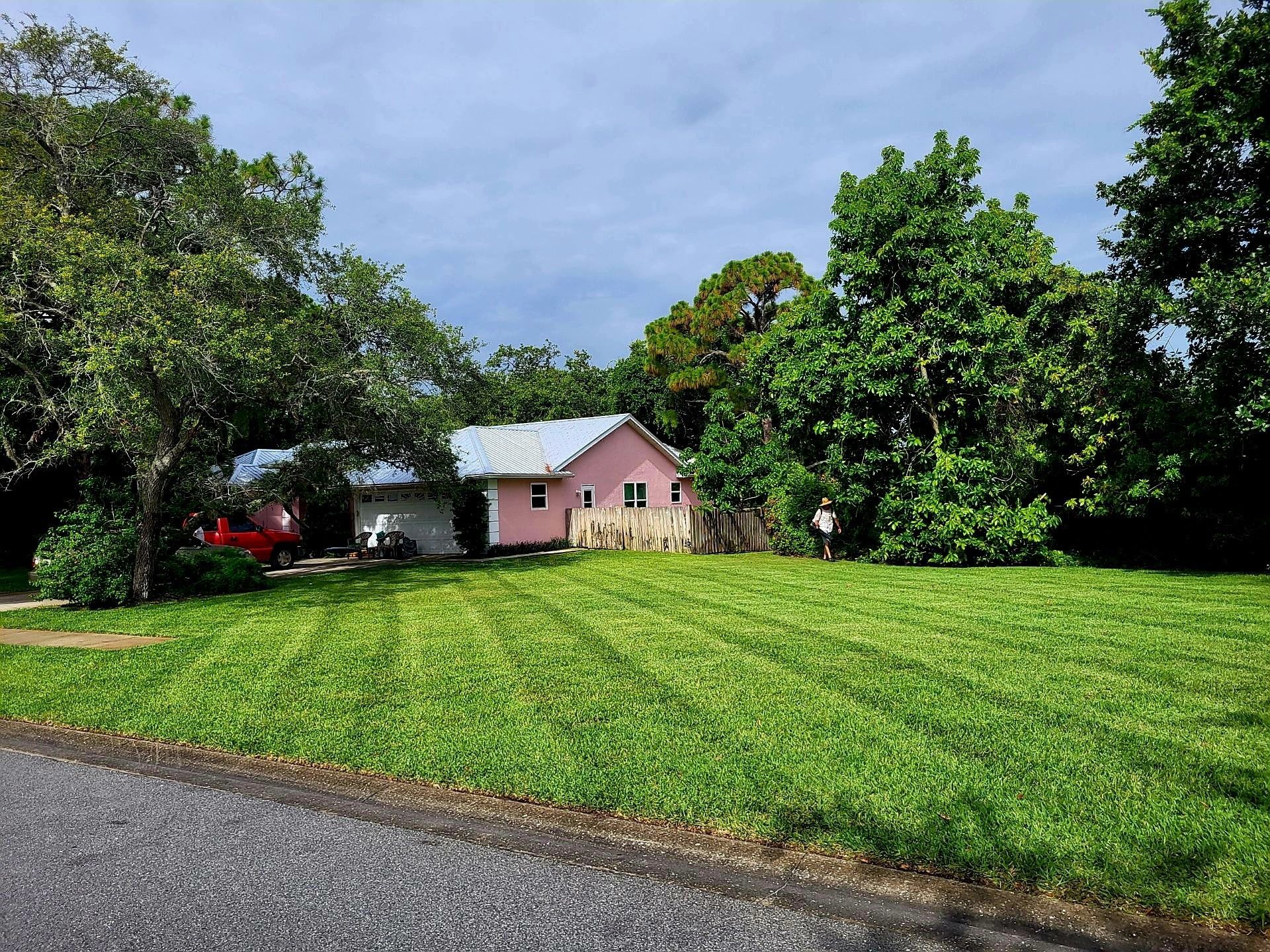 Pink house nestled in lush green yard with a freshly mowed lawn under a cloudy sky.
