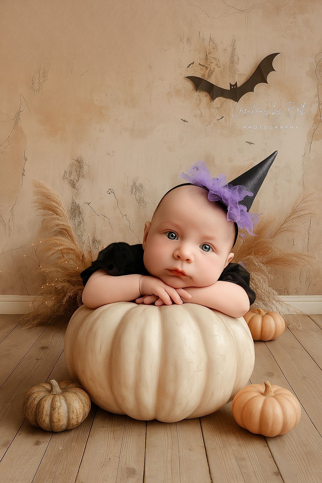 Baby in witch hat leans on a white pumpkin, surrounded by gourds. Halloween setting.