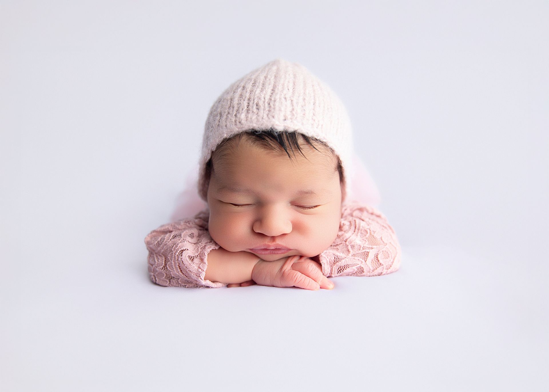 Baby in witch hat leans on white pumpkin, surrounded by pumpkins. Bat decor in background.