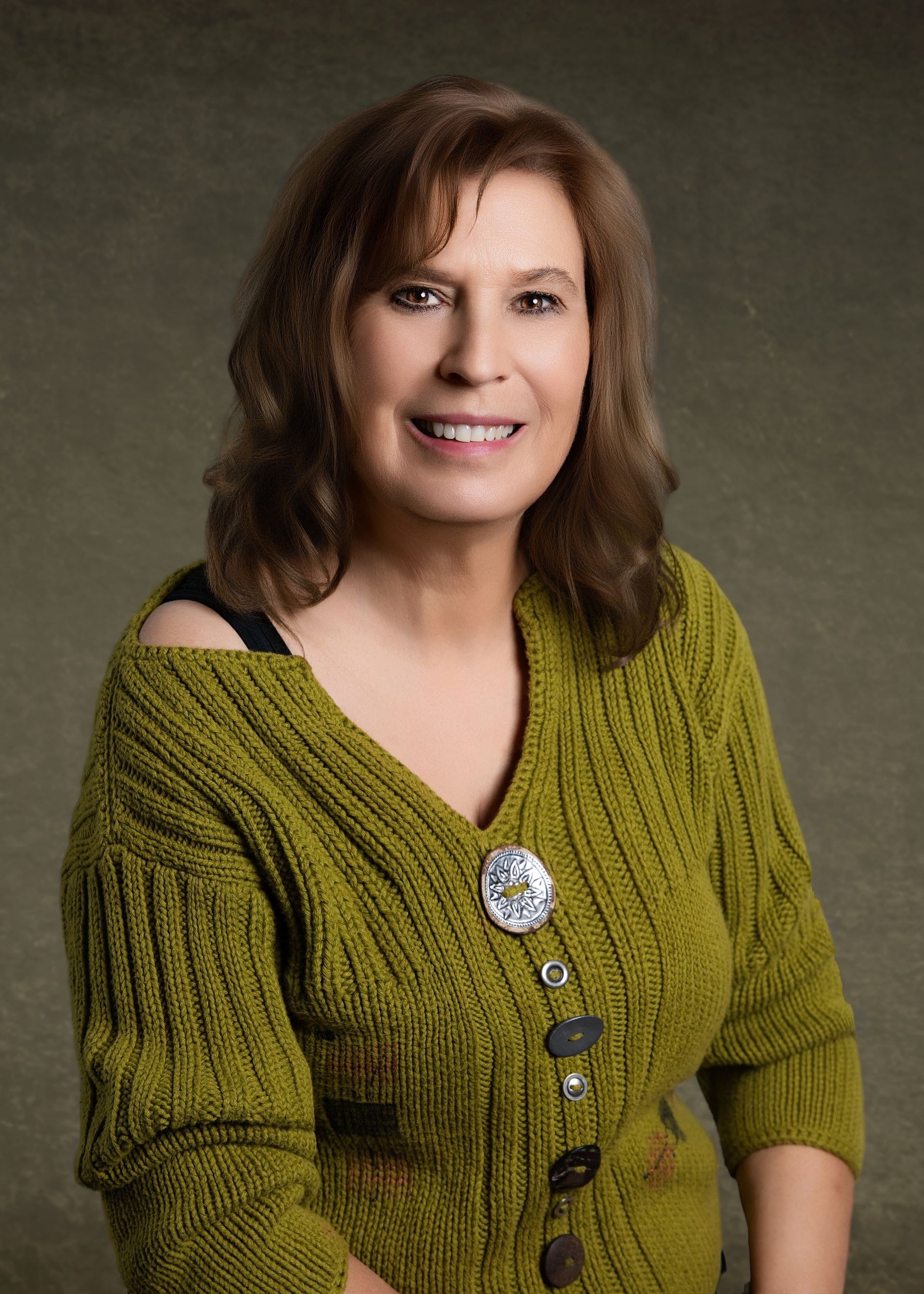 Woman in olive green sweater, smiling, with a brooch on chest.