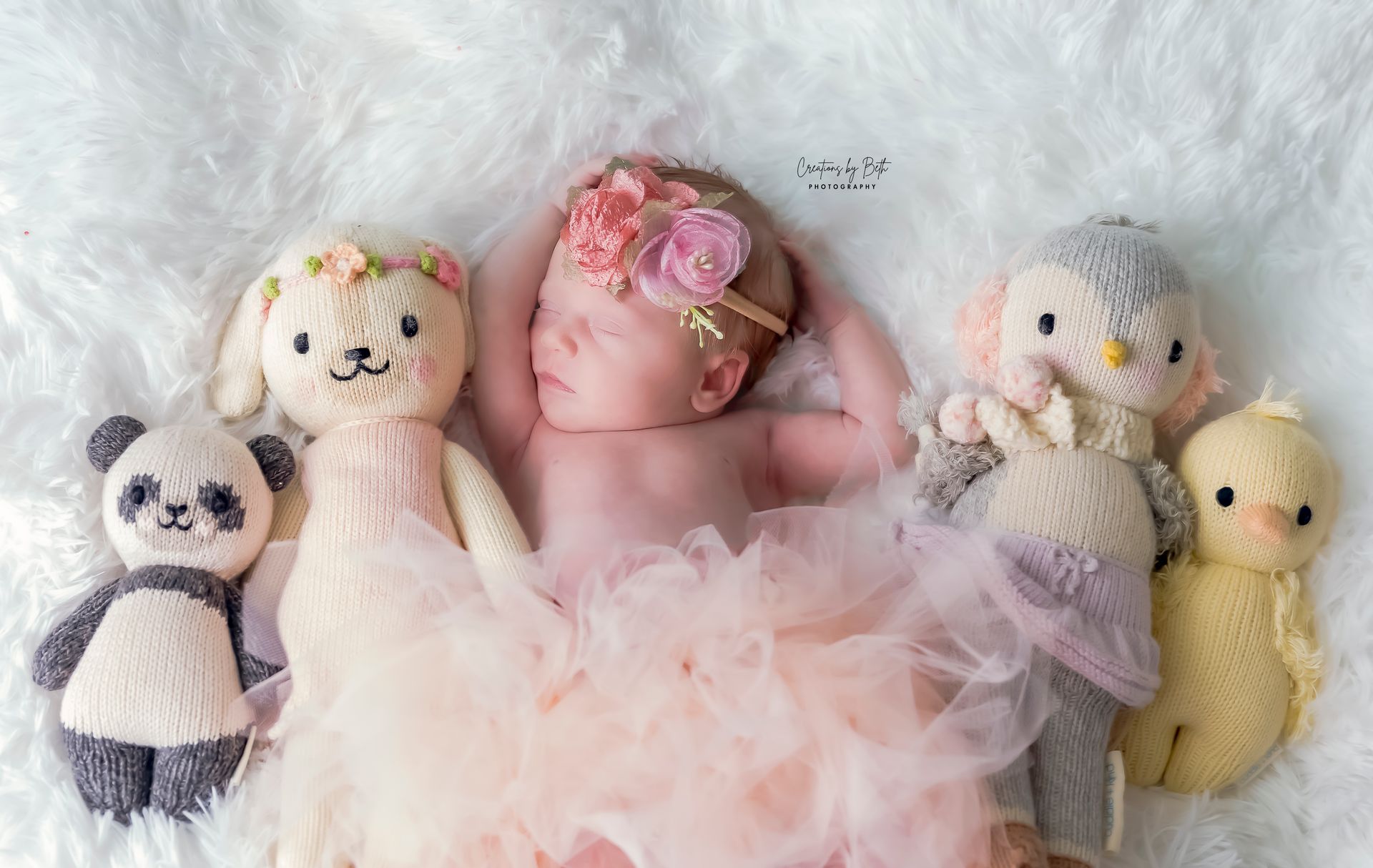 Newborn baby girl wearing pink tutu and flower crown, posed with knitted dolls during newborn photography class