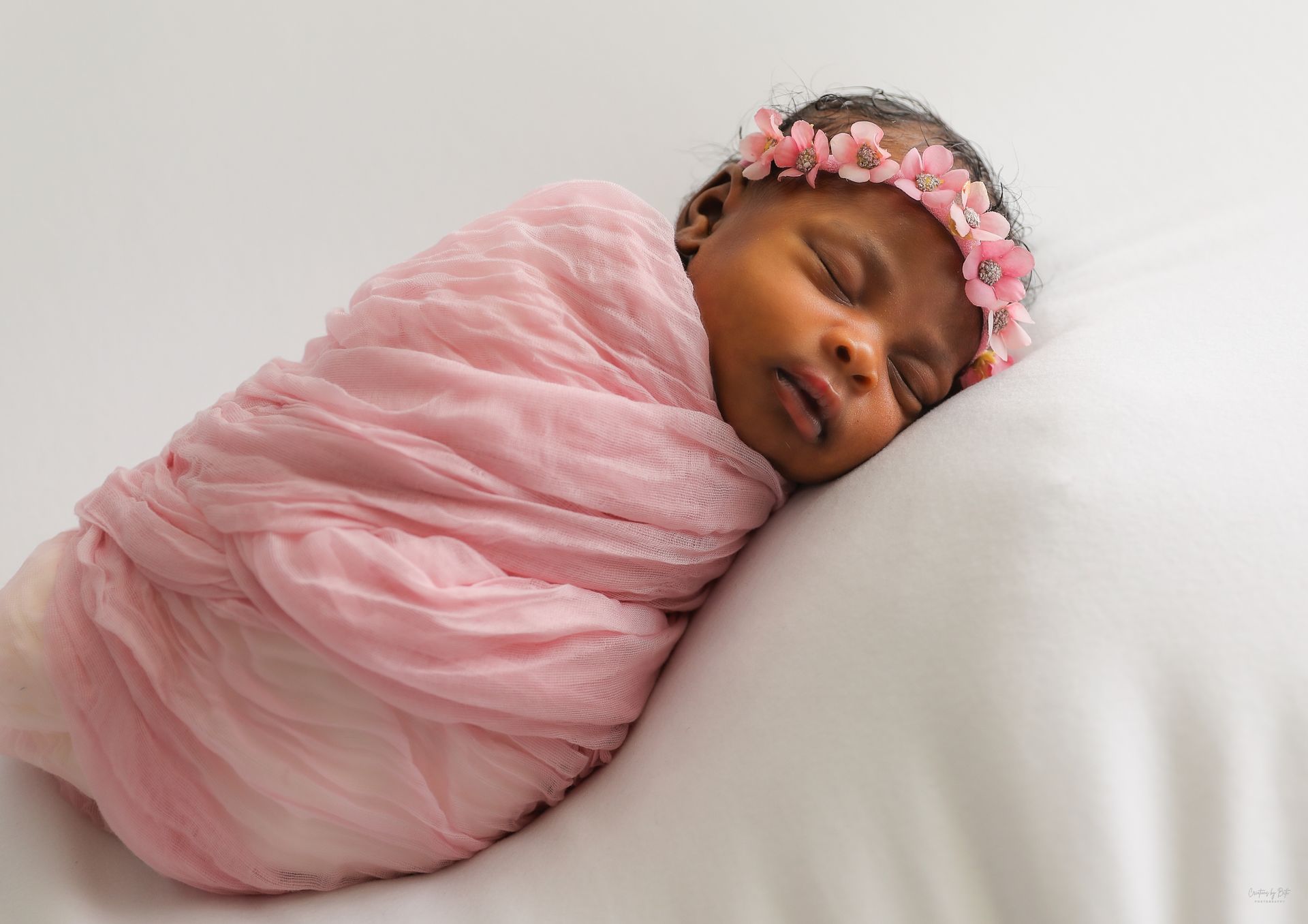 Swaddled newborn girl in pink wrap with floral headband from a hands-on baby photography class