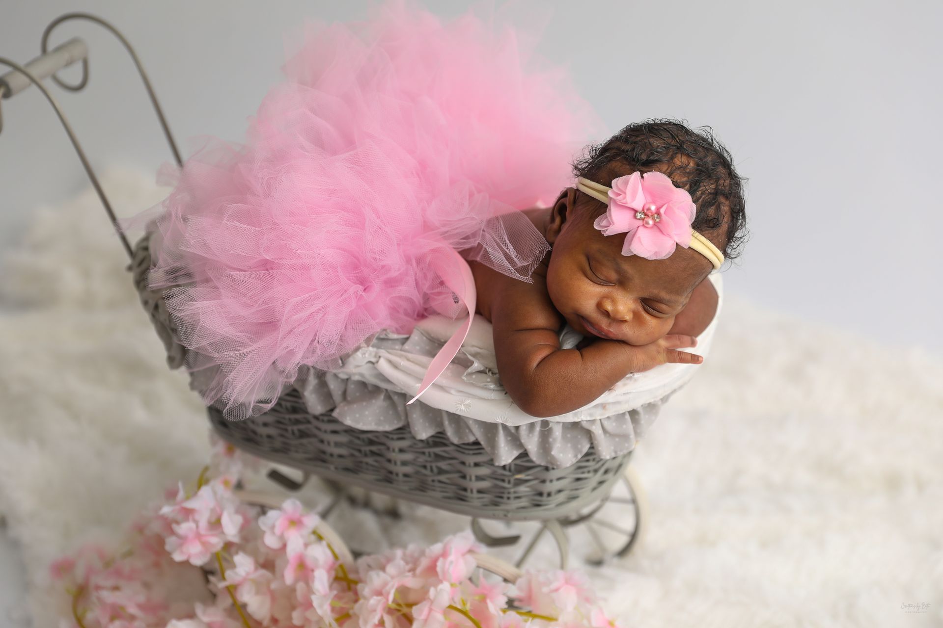A newborn baby girl wearing a pink tutu is sleeping in a stroller.