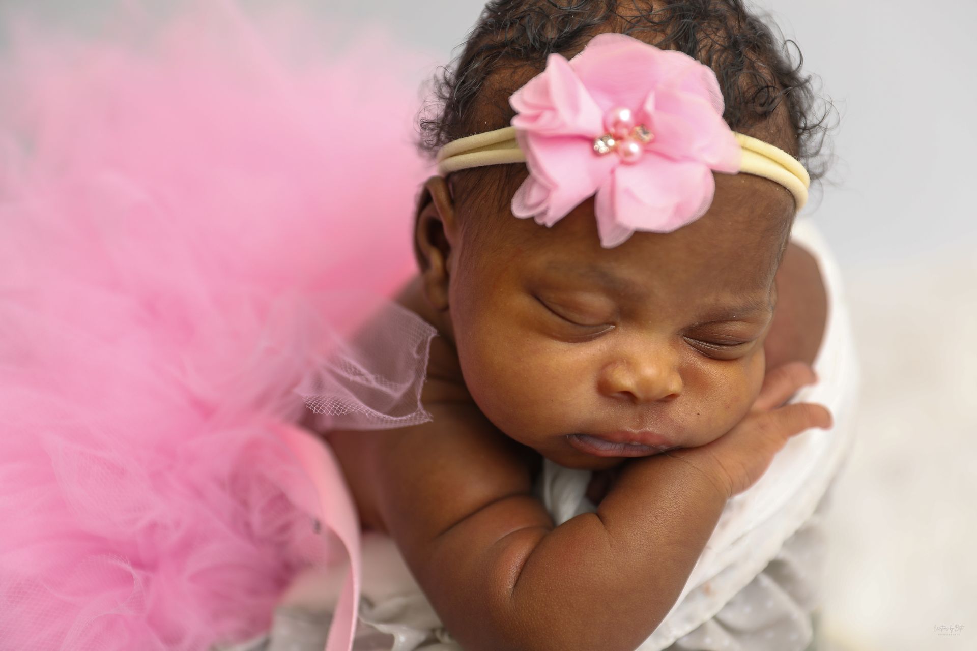 A newborn baby girl wearing a pink tutu is sleeping in a stroller.