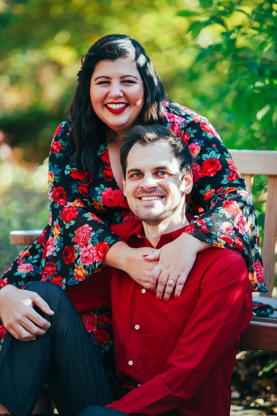 A smiling couple poses outdoors on a bench